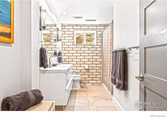 279 Green Meadow Ln, Boulder, CO 80302 - bathroom featuring a textured wall, vanity, toilet, a shower, and stone tile flooring