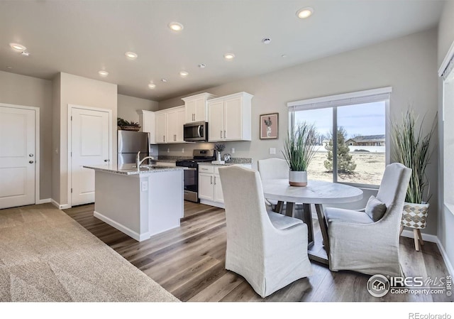 187 Robin Rd, Johnstown, CO 80534 - kitchen with stainless steel appliances, a center island with sink, white cabinetry, wood finished floors, and baseboards
