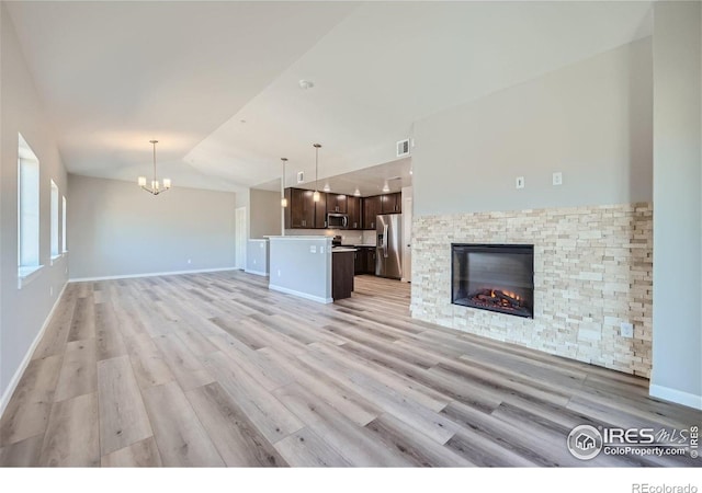 2435 Calais Dr Unit G, Longmont, CO 80504 - unfurnished living room featuring light wood finished floors, vaulted ceiling, a stone fireplace, a chandelier, and baseboards