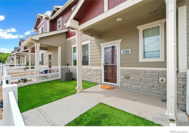 259 Molinar St, Johnstown, CO 80534 - entrance to property featuring a porch, stone siding, a lawn, and central AC