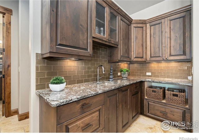 5709 Old Legacy Dr, Fort Collins, CO 80528 - kitchen featuring light stone countertops, decorative backsplash, glass insert cabinets, and dark brown cabinetry