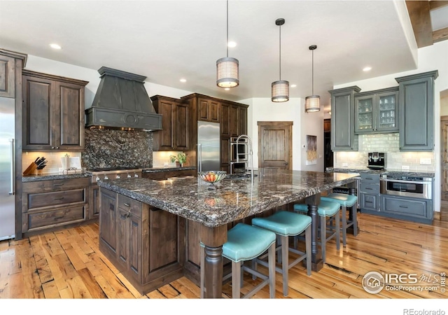 5709 Old Legacy Dr, Fort Collins, CO 80528 - kitchen with premium range hood, tasteful backsplash, light wood finished floors, appliances with stainless steel finishes, and a kitchen bar
