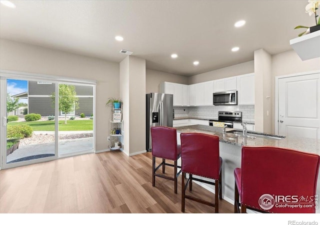 3635 Ronald Reagan Ave, Wellington, CO 80549 - kitchen featuring stainless steel appliances, light wood-style floors, white cabinetry, backsplash, and light stone countertops