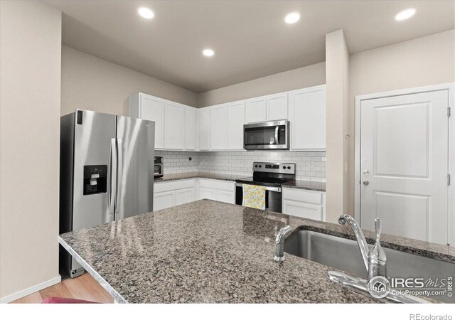 3635 Ronald Reagan Ave, Wellington, CO 80549 - kitchen with stainless steel appliances, white cabinets, dark stone counters, backsplash, and light wood-type flooring