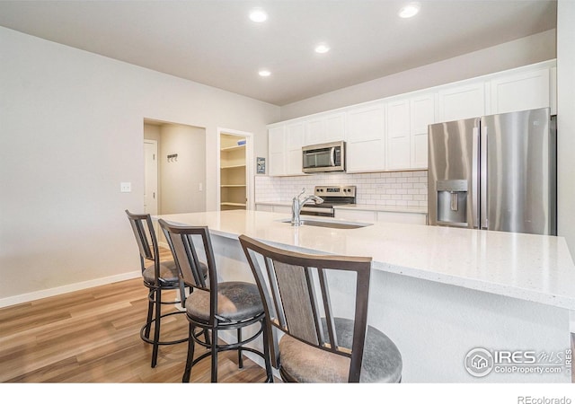 3960 Sweetgum St, Wellington, CO 80549 - kitchen with appliances with stainless steel finishes, a sink, light wood-type flooring, white cabinets, and decorative backsplash
