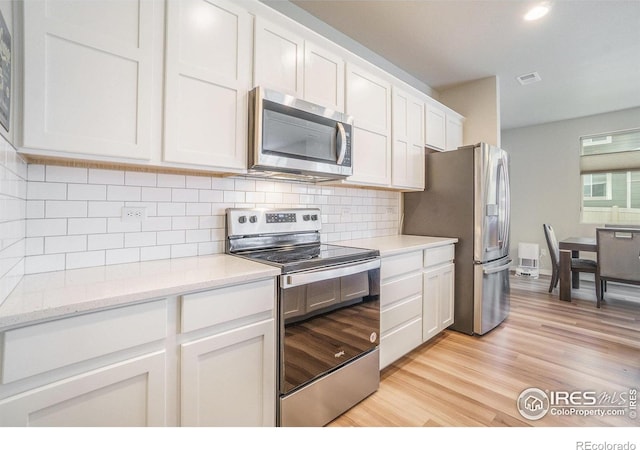 3960 Sweetgum St, Wellington, CO 80549 - kitchen featuring appliances with stainless steel finishes, white cabinetry, decorative backsplash, light wood finished floors, and light stone countertops