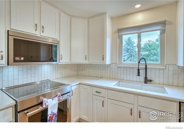 10940 Utica Ct, Westminster, CO 80031 - kitchen featuring appliances with stainless steel finishes, a sink, white cabinetry, decorative backsplash, and recessed lighting