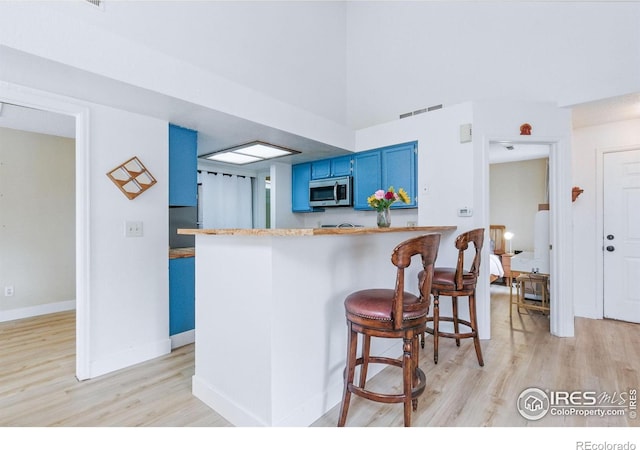 6076 Gunbarrel Ave Unit F, Boulder, CO 80301 - kitchen featuring blue cabinetry, stainless steel microwave, light wood-type flooring, a breakfast bar, and a peninsula