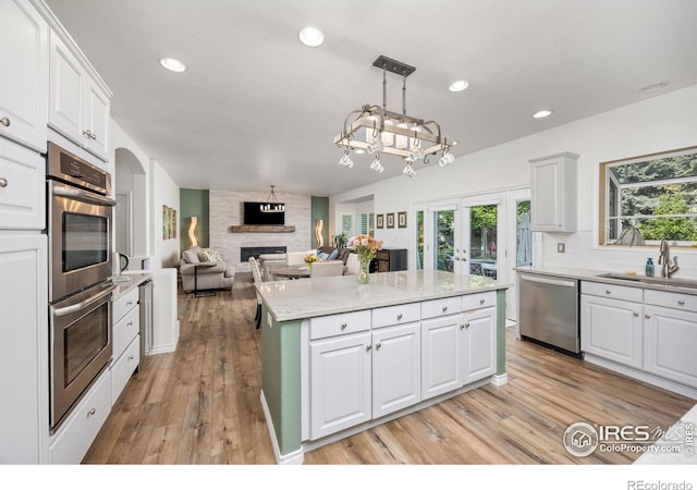 1892 Bell Dr, Erie, CO 80516 - kitchen with appliances with stainless steel finishes, a sink, a large fireplace, a kitchen island, and white cabinetry