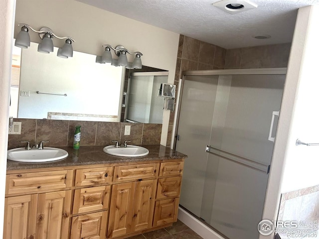 33180 Pikes Peak Dr, Greeley, CO 80631 - bathroom featuring a shower stall, double vanity, decorative backsplash, a textured ceiling, and tile patterned floors