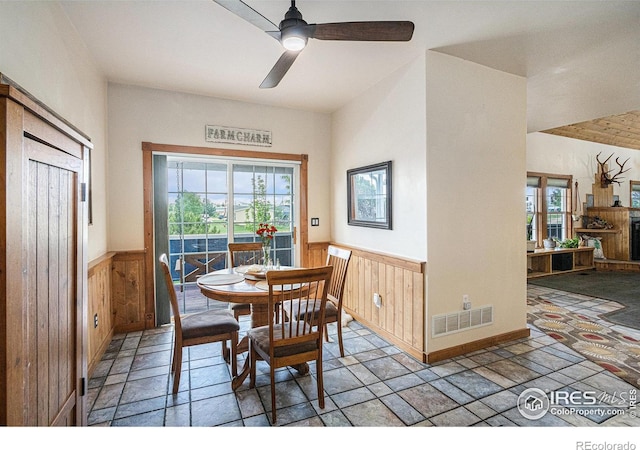 39445 Main St, Eaton, CO 80615 - dining area featuring wainscoting, healthy amount of natural light, ceiling fan, wooden walls, and stone tile floors