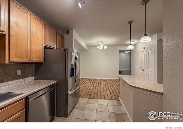 804 Summer Hawk Dr Unit 105, Longmont, CO 80504 - kitchen with appliances with stainless steel finishes, backsplash, decorative light fixtures, light countertops, and brown cabinets