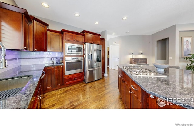 6945 N Fargo Trl, Littleton, CO 80125 - kitchen with appliances with stainless steel finishes, light wood finished floors, dark stone countertops, recessed lighting, and tasteful backsplash