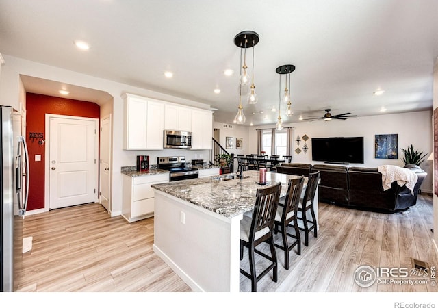 1191 Horsetail Loop, Elizabeth, CO 80107 - kitchen featuring appliances with stainless steel finishes, a breakfast bar area, ceiling fan, light wood-style floors, and light stone countertops