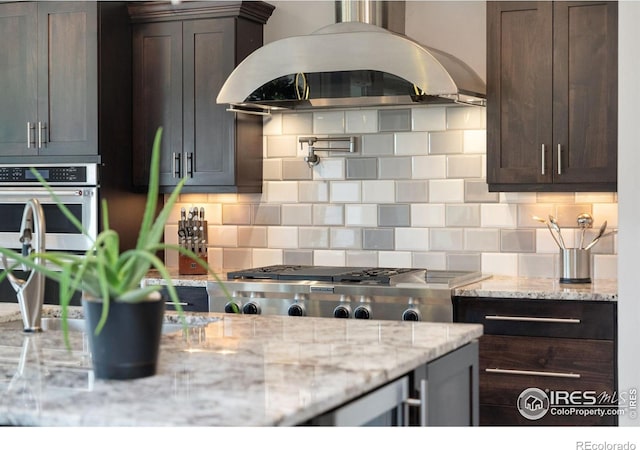 5966 Sunny Crest Dr, Timnath, CO 80547 - kitchen with island range hood, dark brown cabinetry, decorative backsplash, and light stone countertops