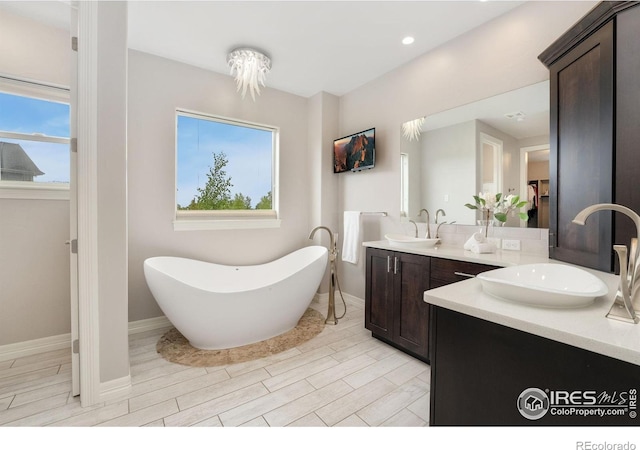 5966 Sunny Crest Dr, Timnath, CO 80547 - bathroom featuring double vanity, a freestanding tub, wood finished floors, baseboards, and recessed lighting