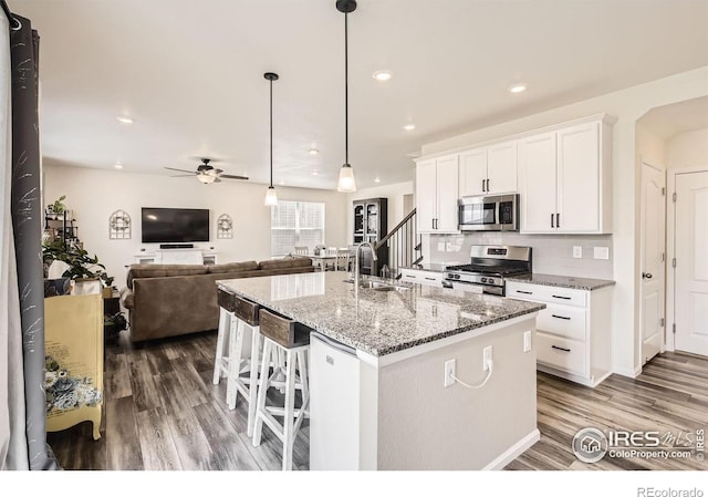 12889 Clearview St, Firestone, CO 80504 - kitchen featuring appliances with stainless steel finishes, wood finished floors, ceiling fan, white cabinets, and light stone counters