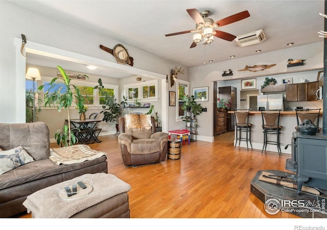 4900 W 6th Ave, Denver, CO 80204 - living room featuring a ceiling fan, light wood-style flooring, a wood stove, a wall mounted AC, and baseboards
