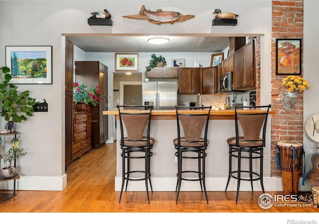 4900 W 6th Ave, Denver, CO 80204 - kitchen featuring stainless steel appliances, a peninsula, a kitchen bar, light wood finished floors, and dark brown cabinetry