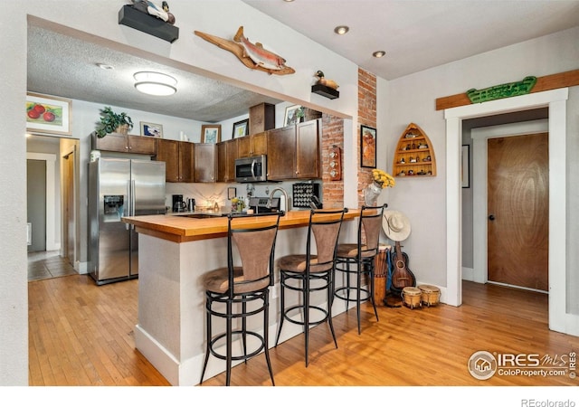 4900 W 6th Ave, Denver, CO 80204 - kitchen with stainless steel appliances, wood counters, light wood-type flooring, a peninsula, and a breakfast bar area