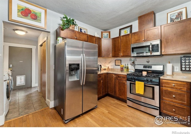 4900 W 6th Ave, Denver, CO 80204 - kitchen with stainless steel appliances, light countertops, light wood finished floors, washer / dryer, and a textured ceiling