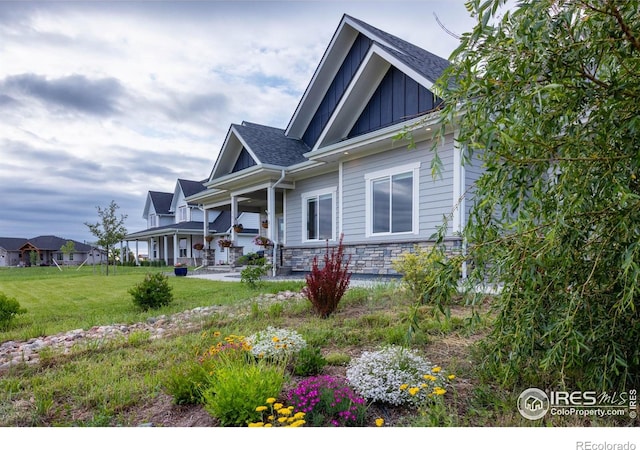 505 Nesting Eagles Way, Berthoud, CO 80513 - view of side of property featuring board and batten siding, a lawn, covered porch, roof with shingles, and stone siding