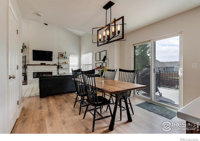 5609 Mount Sanitas Ave, Longmont, CO 80503 - dining room with light wood-style flooring, a chandelier, a glass covered fireplace, and high vaulted ceiling