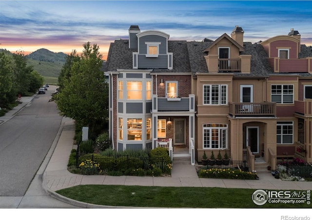 555 Laramie Blvd, Boulder, CO 80304 - back of property at dusk featuring a balcony, a shingled roof, a chimney, brick siding, and a mountain view