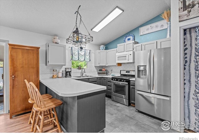 110 50th Ave, Greeley, CO 80634 - kitchen featuring appliances with stainless steel finishes, a peninsula, tasteful backsplash, lofted ceiling, and a kitchen bar