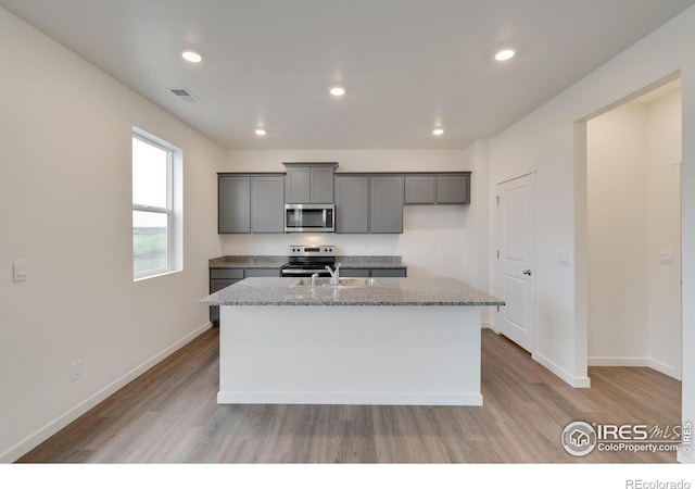 1639 Pinnacle Ave, Lochbuie, CO 80603 - kitchen with stainless steel appliances, light wood-style flooring, an island with sink, gray cabinets, and recessed lighting