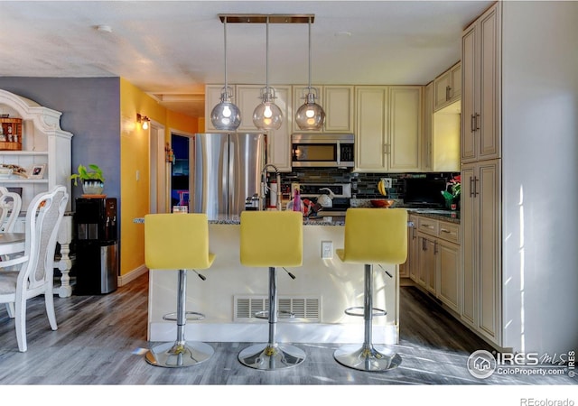 7970 Wolff Ct, Westminster, CO 80030 - kitchen featuring cream cabinets, appliances with stainless steel finishes, decorative backsplash, a kitchen breakfast bar, and wood finished floors