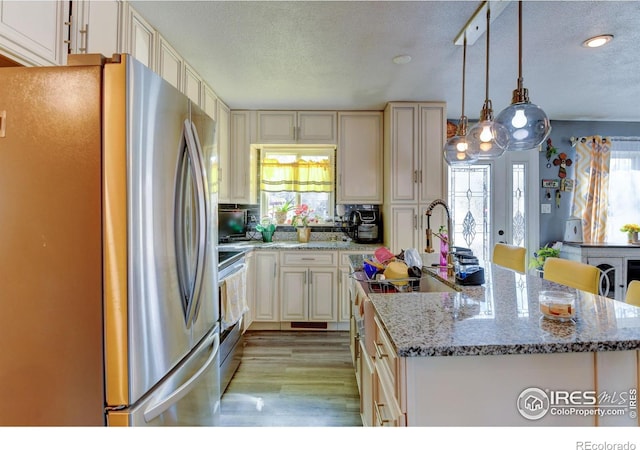 7970 Wolff Ct, Westminster, CO 80030 - kitchen with appliances with stainless steel finishes, a textured ceiling, a kitchen island with sink, light wood-style floors, and light stone countertops