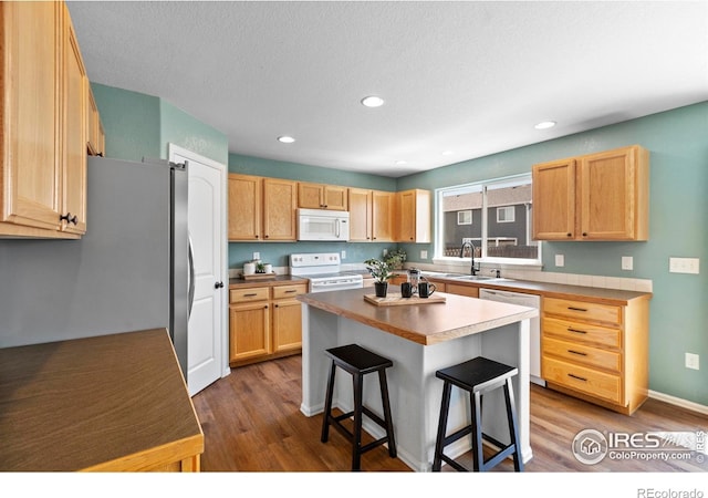 7266 Andover St, Wellington, CO 80549 - kitchen with white appliances, a breakfast bar area, wood finished floors, a kitchen island, and recessed lighting