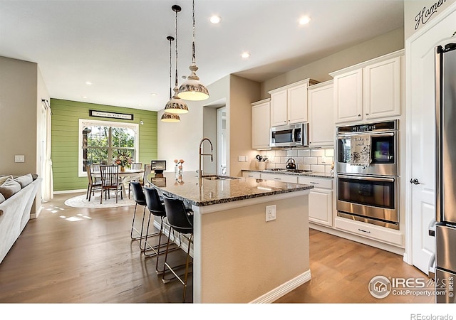 2050 Vineyard Dr, Windsor, CO 80550 - kitchen with stainless steel appliances, wood finished floors, a breakfast bar area, white cabinetry, and dark stone countertops