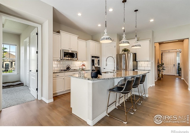 2050 Vineyard Dr, Windsor, CO 80550 - kitchen with stainless steel appliances, wood finished floors, an island with sink, tasteful backsplash, and recessed lighting