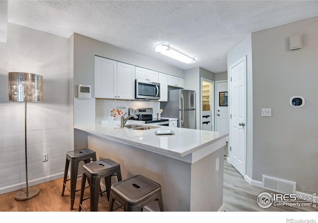 4763 White Rock Cir Unit A, Boulder, CO 80301 - kitchen featuring stainless steel appliances, light wood finished floors, a kitchen breakfast bar, white cabinets, and a textured ceiling