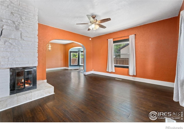 556 Lincoln Ave, Nunn, CO 80648 - unfurnished living room featuring arched walkways, ceiling fan, wood finished floors, and a stone fireplace