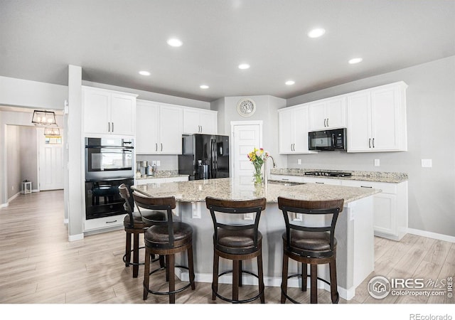 973 Mt Andrew Dr, Severance, CO 80550 - kitchen featuring black appliances, light wood finished floors, a kitchen island with sink, a breakfast bar, and recessed lighting