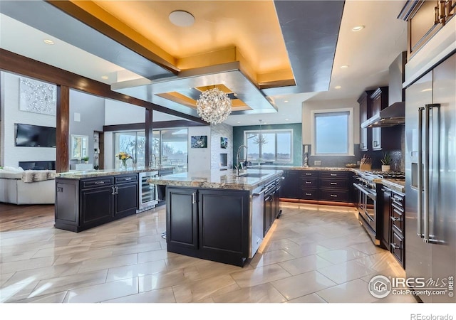 5763 Pelican Shores Dr, Longmont, CO 80504 - kitchen featuring high quality appliances, an island with sink, beverage cooler, a chandelier, and wall chimney range hood