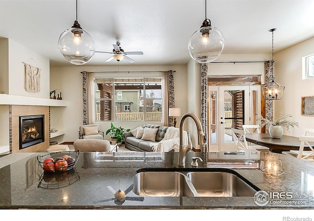 5457 Wishing Well Dr, Timnath, CO 80547 - kitchen featuring a tile fireplace, dark stone counters, hanging light fixtures, and a ceiling fan