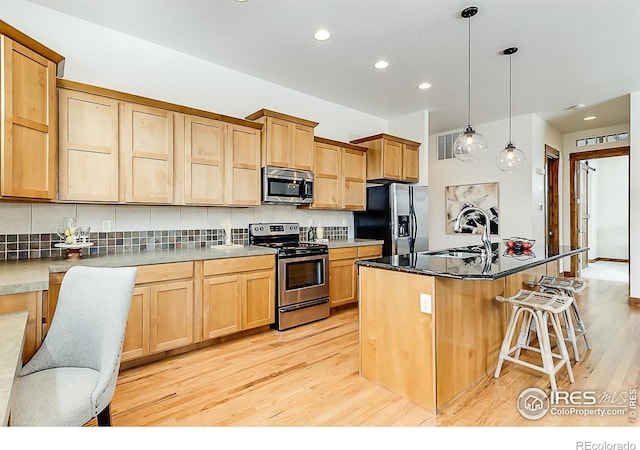 5457 Wishing Well Dr, Timnath, CO 80547 - kitchen featuring appliances with stainless steel finishes, light wood-type flooring, a kitchen bar, recessed lighting, and decorative backsplash