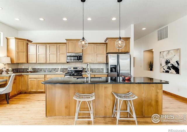 5457 Wishing Well Dr, Timnath, CO 80547 - kitchen with appliances with stainless steel finishes, light wood-style floors, backsplash, a kitchen island with sink, and recessed lighting