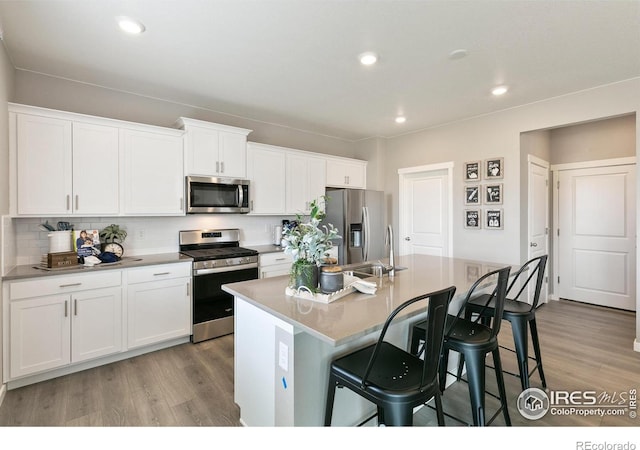 114 65th Ave, Greeley, CO 80634 - kitchen with appliances with stainless steel finishes, light wood-style floors, a breakfast bar area, an island with sink, and recessed lighting