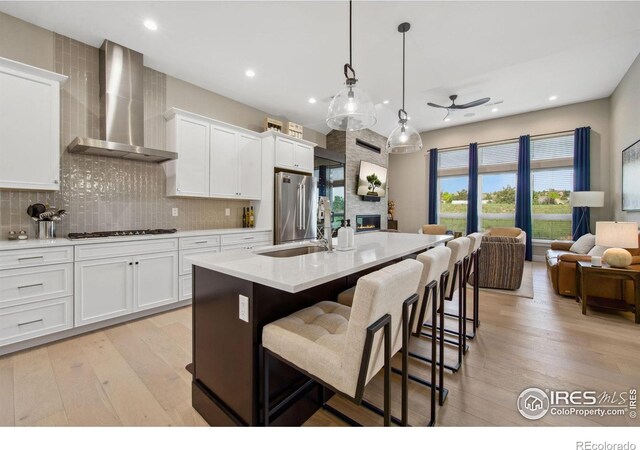1768 Barefoot Dr, Windsor, CO 80550 - kitchen featuring wall chimney range hood, freestanding refrigerator, a ceiling fan, gas stovetop, and a fireplace