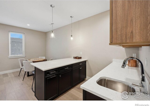 1768 Barefoot Dr, Windsor, CO 80550 - kitchen with light wood-type flooring, a peninsula, dark cabinetry, and decorative light fixtures