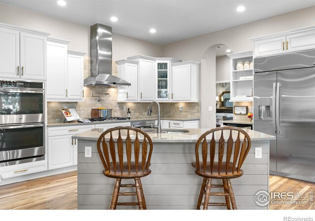 1976 Cayman Dr, Windsor, CO 80550 - kitchen featuring stainless steel appliances, wall chimney exhaust hood, white cabinetry, light wood finished floors, and a breakfast bar