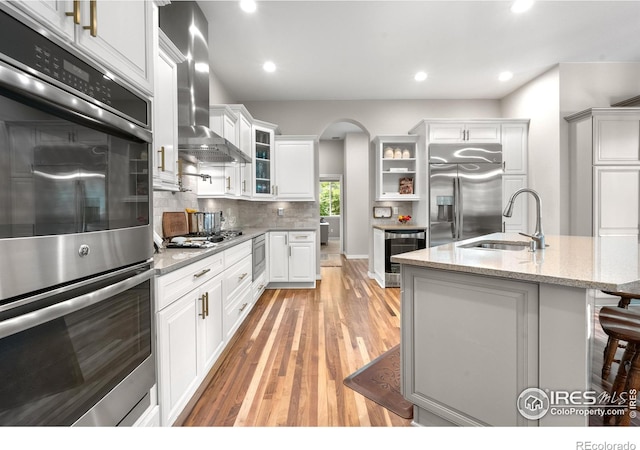 1976 Cayman Dr, Windsor, CO 80550 - kitchen with appliances with stainless steel finishes, arched walkways, wall chimney range hood, wine cooler, and glass insert cabinets