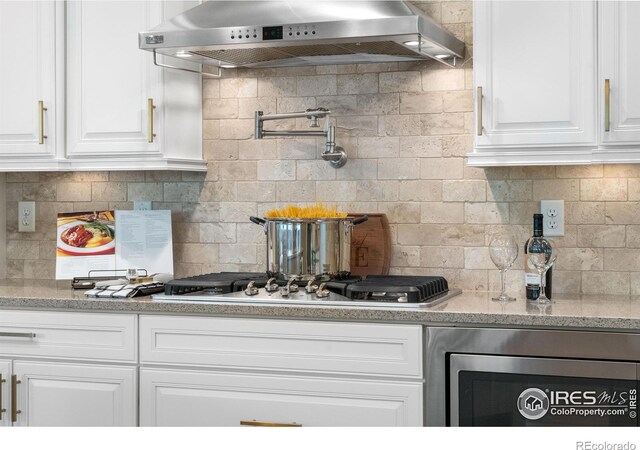 1976 Cayman Dr, Windsor, CO 80550 - kitchen featuring wall chimney range hood, white cabinets, decorative backsplash, and light stone countertops