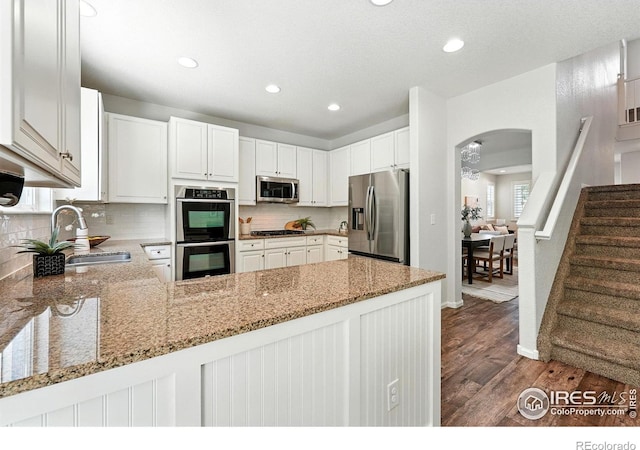 1662 Crestview Ln, Erie, CO 80516 - kitchen featuring stainless steel appliances, dark wood-type flooring, arched walkways, light stone counters, and tasteful backsplash