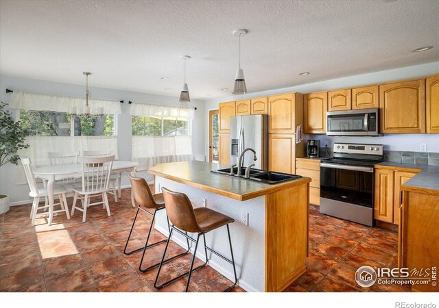 322 W Harper St, Louisville, CO 80027 - kitchen featuring stainless steel appliances, dark countertops, a breakfast bar, a kitchen island with sink, and hanging light fixtures